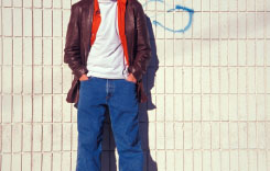young man in jeans leaning against a wall